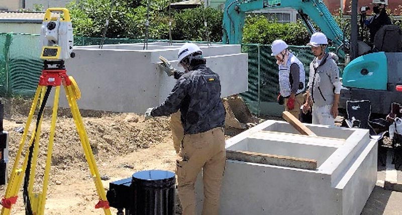 Construction workers installing pre-fabricated concrete foundations on a construction site with a Leica iCON total station
